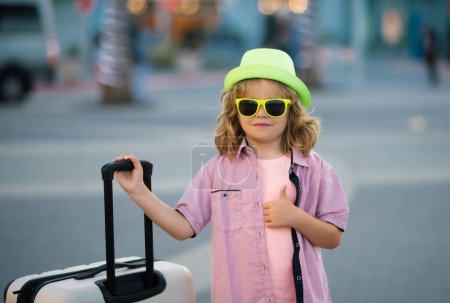 Foto de Divertido viajero infantil. Niño feliz turista con viaje bolsa de viaje. Niño con maleta viajando en la calle de la ciudad al aire libre - Imagen libre de derechos