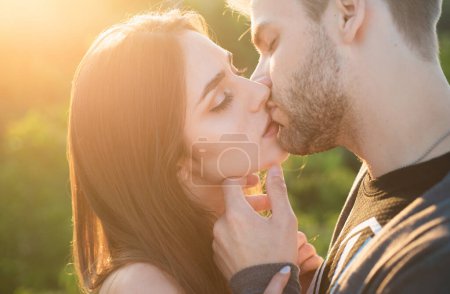 Foto de El primer plano de la joven pareja romántica es besarse. Perfil de personas hermosas enamoradas expresándose y afectuándose mientras se besan con los ojos cerrados al atardecer de otoño - Imagen libre de derechos