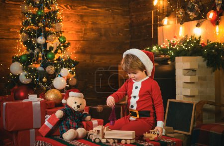 Téléchargez les photos : Happy kid joue avec des jouets de Noël. Le gamin attend le Nouvel An. Chapeau de Père Noël. Vacances - en image libre de droit