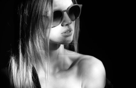 Foto de Retrato de mujer hermosa en modelo de gafas de sol con aspecto seductor y sensual. Cara de belleza con dramática luz de estudio aislada en negro - Imagen libre de derechos