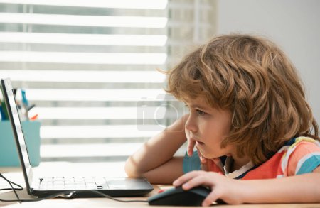 Téléchargez les photos : Portrait d'un écolier regardant l'ordinateur portable pendant la leçon. Premier jour à l'école. Petit enfant mignon étudiant - en image libre de droit