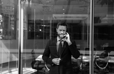 Foto de Hombre de negocios hablando por teléfono. Retrato del trabajador de oficina alegre del empresario que habla en el teléfono móvil mientras que está parado cerca de la oficina moderna - Imagen libre de derechos