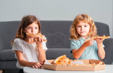 Téléchargez les photos : Joyeux fils et fille mangeant de la pizza. Les enfants les enfants aiment et s'amusent avec le déjeuner ensemble à la maison. Petits amis, garçon et fille mordent pizza - en image libre de droit