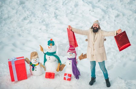 Téléchargez les photos : Noël hiver gens portrait. Préparation de Noël - drôle homme barbu avec boîte cadeau rouge faire bonhomme de neige. Bonne période hivernale - en image libre de droit
