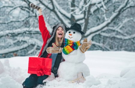 Téléchargez les photos : Portrait de mode de jeune fille modèle à l'intérieur avec bonhomme de neige de Noël. Beauté hiver fille avec bonhomme de neige en hiver givré Parc - en image libre de droit
