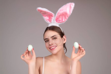 Téléchargez les photos : Portrait d'une jolie jeune femme romantique aux oreilles de lapin célébrant les vacances de Pâques, fond de studio. Concept de fête de vacances. Fille joyeuse célébrant Pâques dans les oreilles de lapin, tenant des œufs peints - en image libre de droit