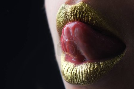 Téléchargez les photos : La langue sexy lèche les lèvres. Peinture dorée sur la bouche. Des lèvres dorées. Maquillage de luxe lèvres dorées. Lèvres dorées avec rouge à lèvres métallique créatif. Lèvre en métal doré. Femme sensuelle bouche, gros plan, macro - en image libre de droit