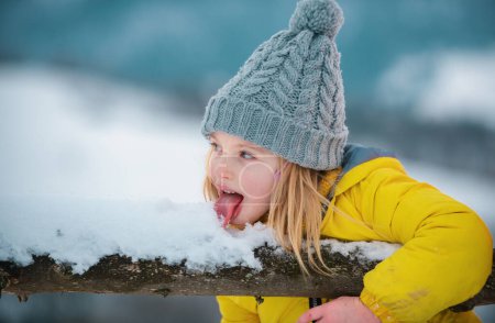 Photo for Winter girl eating snow outdoor. Funny christmas kids lick snow with tongue. Kids cold and flu concept. Children wearing warm winter clothing in snow weather - Royalty Free Image