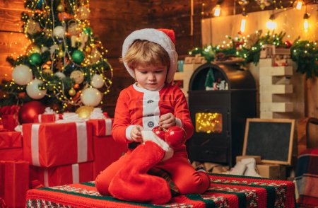 Foto de Feliz niño sonriente con calcetines de regalo de Navidad. Concepto de Año Nuevo. Niño feliz divirtiéndose con el regalo. Árbol de Navidad fondo - Imagen libre de derechos