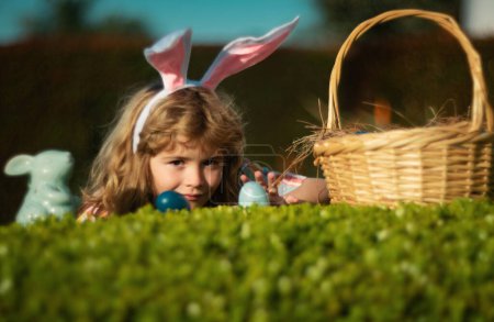 Osterhasenkind auf Eiersuche im Freien Frohe Ostern, Junge liegt auf Gras im Park