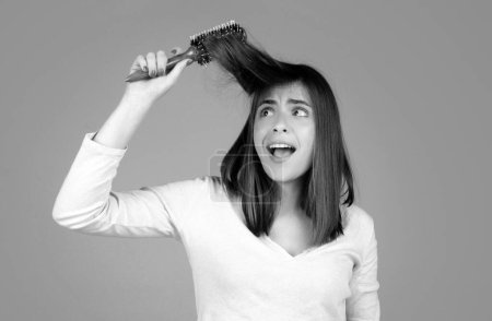 Téléchargez les photos : Femme drôle excitée peigner les cheveux. Portrait de modèle féminin avec un peigne brossant les cheveux. Fille avec brosse à cheveux, soins des cheveux et beauté. Routine matinale - en image libre de droit