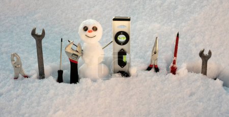 Foto de Herramientas de reparación de constructores. Pequeño muñeco de nieve con instrumento de reparación. Hombre de nieve trabajador - Imagen libre de derechos