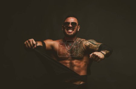 Foto de Un hombre furioso aislado en negro. Camisa rasgada modelo masculino sin camiseta en topless - Imagen libre de derechos