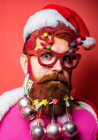 Téléchargez les photos : Père Noël posant sur fond de bois vintage. Le Père Noël souhaite joyeux Noël. Holly joyeux swag Noël et le nez. Portrait d'un Père Noël sur fond rouge isolé - en image libre de droit