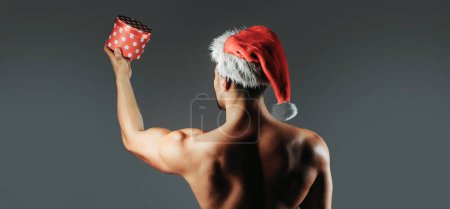 Photo for Christmas sexy man. Young men in santa hat. New year strip and gifts for adults. Muscle man at xmas. Santa with muscular body. Handsome sexy santa claus guy on gray background - Royalty Free Image