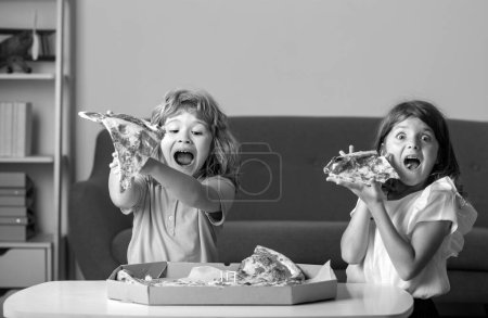 Foto de Niños comiendo pizza. Niños emocionados comiendo pizza. Dos niños pequeños muerden pizza adentro - Imagen libre de derechos