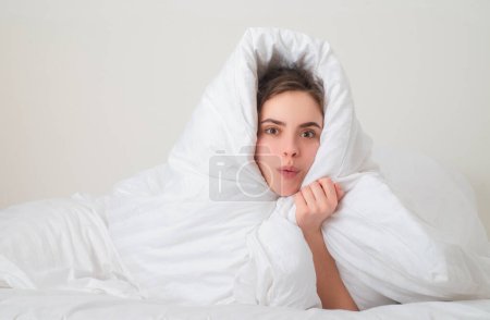 Téléchargez les photos : Femme drôle enveloppée dans une couverture douce assise sur le lit. Fille souriante assise au lit et souriante à la maison - en image libre de droit