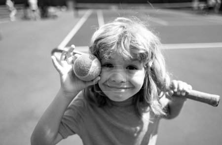 Téléchargez les photos : Petit garçon mignon avec raquette de tennis sur le court à la compétition de tennis. Visage drôle d'enfants - en image libre de droit