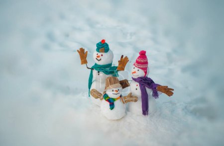 Photo for New Year banner. Funny group of snowmen family in stylish hat and scarf on snowy field. New Year greeting card. Happy snowman couple and snowman child standing in winter Christmas landscape - Royalty Free Image