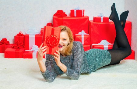 Photo for Glamour celebration. Christmas fashion. Smiling beautiful young girl holding red present box. Sexy Santa Clause woman in elegant dress. Sexy woman. New year girl. Sensual young girl - Royalty Free Image