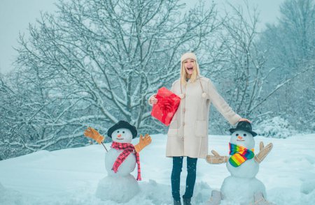 Téléchargez les photos : Émotion hivernale. Vêtements d'hiver pour femme. Fille heureuse jouant avec un bonhomme de neige sur une promenade hivernale enneigée. Matin d'hiver - en image libre de droit