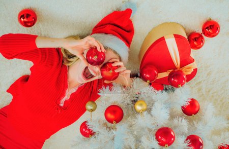Téléchargez les photos : Bonne humeur jeune femme portant le costume de Noël sur la paroi en bois. Belle femme avec gif boîte de Noël à la maison. Émotion heureuse - en image libre de droit