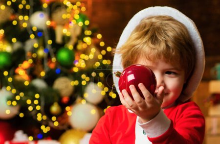 Téléchargez les photos : Joyeux petit garçon regardant Noël bauple. Concept Nouvel An - Portrait d'enfant de Noël. Boule de Noël - en image libre de droit
