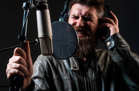 Téléchargez les photos : Un chanteur dans un studio d'enregistrement. Homme barbu expressif avec microphone. Signataire karaoké, chanteur musical - en image libre de droit