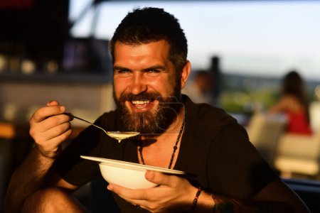 Photo for Man eat soup. Good Appetite. Bearded man with bowl of soup. Happy guy eating soup outdoor. Man eating delicious soup in restaurant. Dinner and meal. Man eating lunch in a cafe - Royalty Free Image
