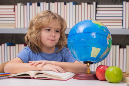 Téléchargez les photos : School pupil looking at globe in library at the elementary school. World globe. Kid boy from elementary school with book. Concept of education and learning - en image libre de droit