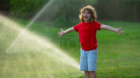 Photo for Child play in summer garden. Grass watering. Automatic sprinkler irrigation system in a green park watering lawn. Sprinkler watering. Child gardening concept. Little kid having fun on water spraying - Royalty Free Image