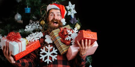 Téléchargez les photos : Un homme incroyable avec un don. Hipster homme en chapeau de Père Noël et pull d'hiver s'amuser. Guy visage heureux avec cadeau - en image libre de droit