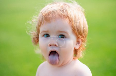 Photo for Funny child in park. Baby face with tongue close up. Funny little child closeup portrait. Blonde kid, emotion face - Royalty Free Image