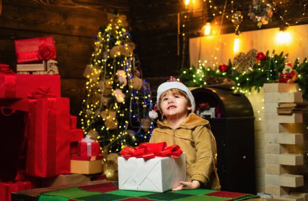 Foto de El niño de Navidad quiere saber qué hay dentro de la caja de regalo de Navidad. Feliz niño sonriente con caja de regalo de Navidad. Concepto de vacaciones. Curioso. - Imagen libre de derechos