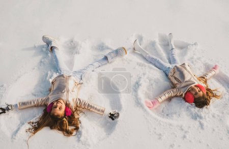 Téléchargez les photos : Des enfants souriants couchés sur la neige avec de l'espace pour copier. Des enfants drôles qui font des anges des neiges. Enfants jouant et faisant un ange de neige dans la neige. Vue du dessus - en image libre de droit
