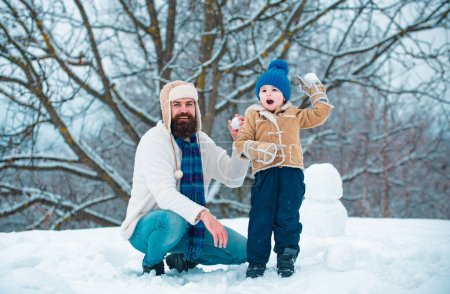 Téléchargez les photos : Père et fils jouent avec boule de neige sur fond blanc d'hiver. Vacances de Noël et nouvel an d'hiver avec père et fils - en image libre de droit