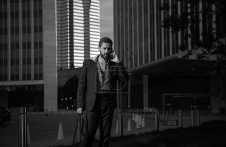 Téléchargez les photos : Homme d'affaires moderne parlant au téléphone à l'extérieur avec paysage urbain en arrière-plan - en image libre de droit
