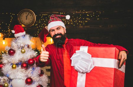 Téléchargez les photos : Homme de Noël dans la mode robe rouge tenir cadeau. Cadeau créatif. Hipster Santa Claude. Noël Père Noël avec cadeau - en image libre de droit
