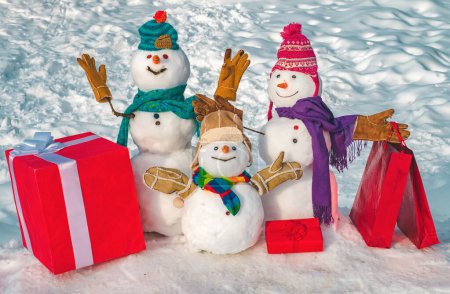 Téléchargez les photos : Joyeux couple bonhomme de neige et enfant bonhomme de neige avec cadeau de Noël debout dans le paysage de Noël d'hiver. Carte de voeux du Nouvel An. Joyeux Noël et bonne année carte de voeux - en image libre de droit