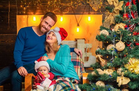 Photo for The morning before Christmas for happy family. Happy family by the Christmas tree. Baby is opening a christmas gift. Lovely parents on the Christmas background - Royalty Free Image