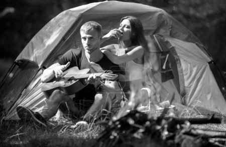 Photo for Carefree coupl near campfire bonfire, freedom concept. Girlfriend and boyfriend on romantic weekend in nature. Couples lovers camping in forest in summer time, man with guitar - Royalty Free Image