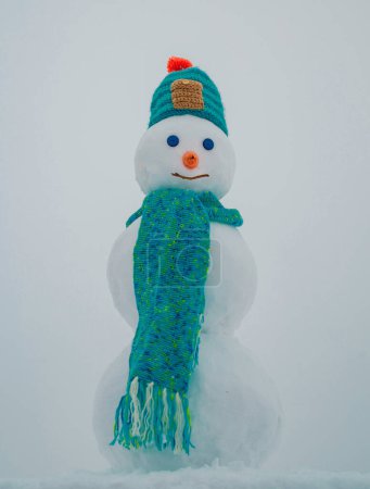 Téléchargez les photos : Bonhomme de neige. Vêtements d'hiver, bonnet tricoté et écharpe. Bonhomme de neige isolé sur fond de neige - en image libre de droit