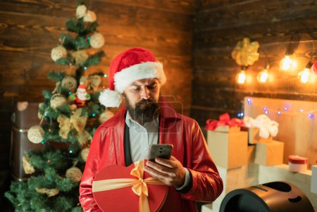 Téléchargez les photos : Santa tenir mobil et souhaite Joyeux Noël et Bonne année. Santa Claude avec boîte cadeau de Noël rouge - en image libre de droit