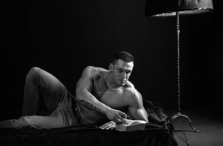 Téléchargez les photos : Sexy homme nu attrayant avec corps nu dans le lit la lecture d'un livre. Concept gay de nuit. Concept bien-être, bien-être - en image libre de droit