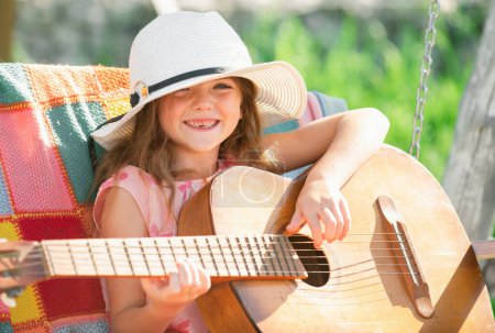 Téléchargez les photos : Enfant musicien jouant de la guitare. Petite fille chantant et jouant de la guitare dehors. Musique et chansons pour enfants. Enfant souriant jouant à l'extérieur en été - en image libre de droit