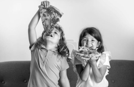Foto de Niños graciosos comiendo pizza. Lindos niños niña y niño comiendo sabrosa pizza - Imagen libre de derechos