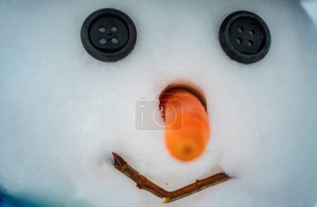Foto de Happy funny snowman in the snow. New year Christmas concept. Snowman with red nose and black eyes button - Imagen libre de derechos