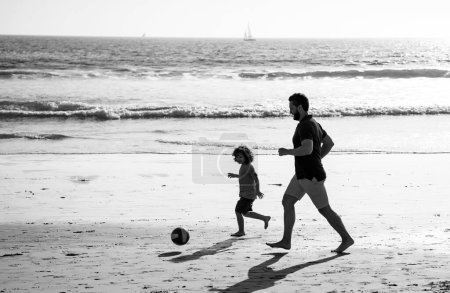 Téléchargez les photos : Père et fils jouent au football ou au football sur la plage. Papa et enfant profitant de plein air. Style de vie et vacances en famille, bonheur concept hommes - en image libre de droit