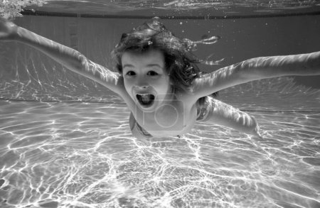 Foto de Muchacho excitado nada bajo el agua en la piscina. Niño bajo el agua. Divertido retrato facial de niño nadando y buceando bajo el agua con diversión en la piscina. Diversión de verano con niños. Vacaciones familiares de verano - Imagen libre de derechos