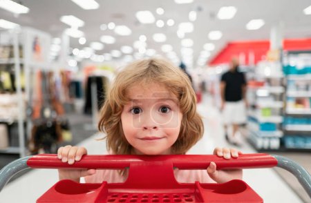 Téléchargez les photos : Enfant avec panier dans une épicerie. Enfant drôle avec panier achetant de la nourriture à l'épicerie ou au supermarché. Visage surprenant des enfants - en image libre de droit